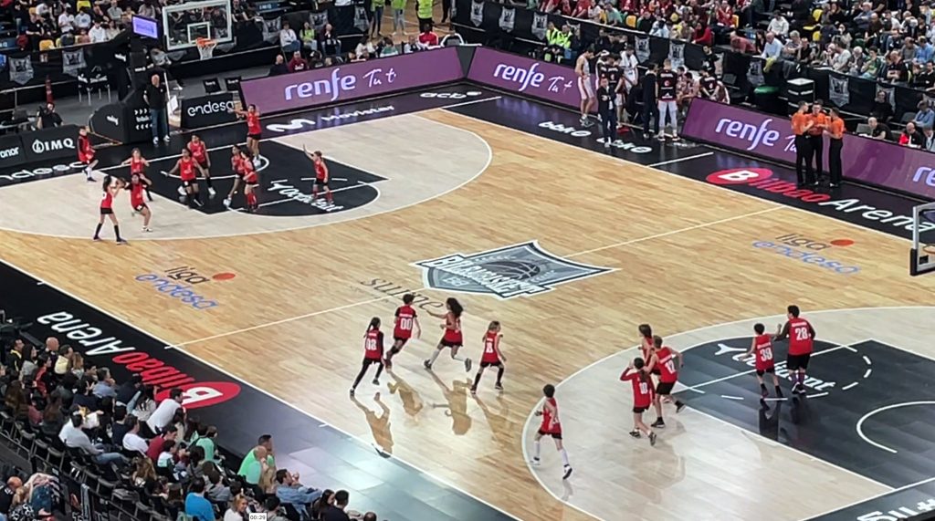 Equipos de mini y premini de baloncesto de CEIP Cervantes HLHI en la cancha del Bilbao Basket. Foto cenital en la que se ve a los equipos jugando en cada una de las dos canastas. Todos con camisetas rojas.